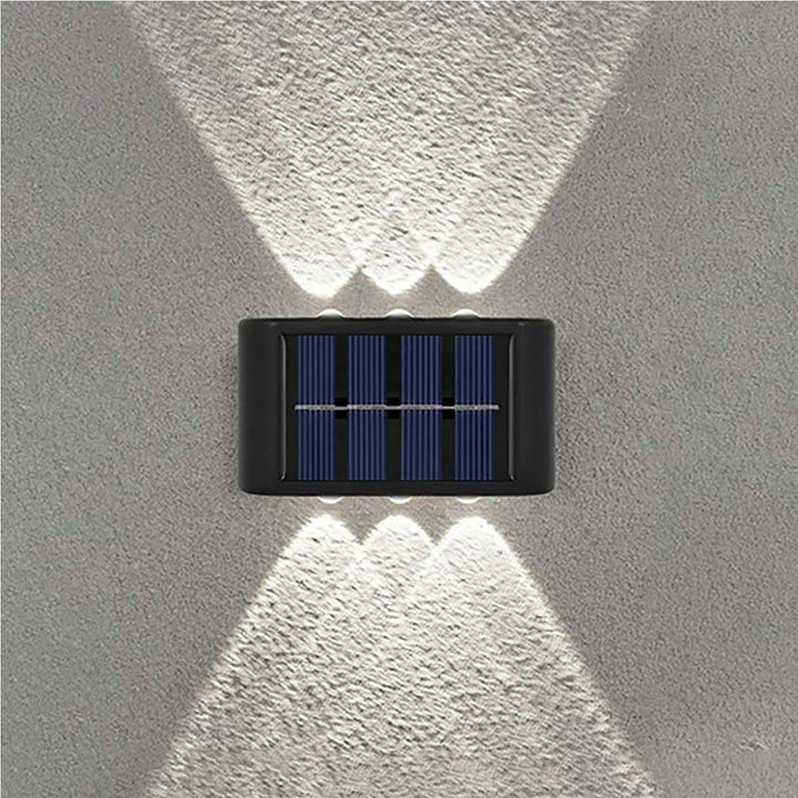 Symmetrical dual-beam solar wall lamp casting stylish white light effect on textured outdoor wall. 