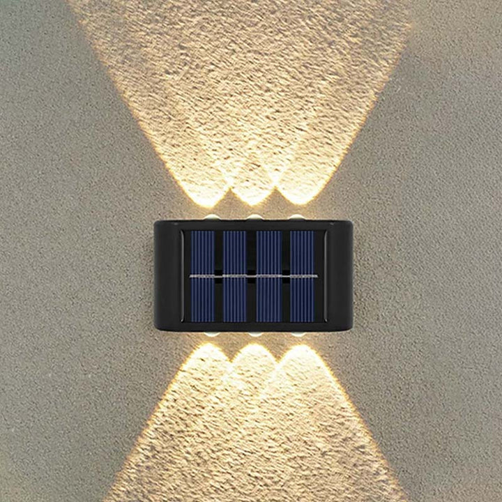 Symmetrical dual-beam solar wall lamp casting stylish wwrm light effect on textured outdoor wall.