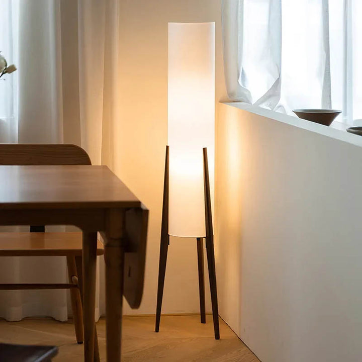 HOJ wooden frame floor lamp in dining corner, casting warm vertical light against the wall.