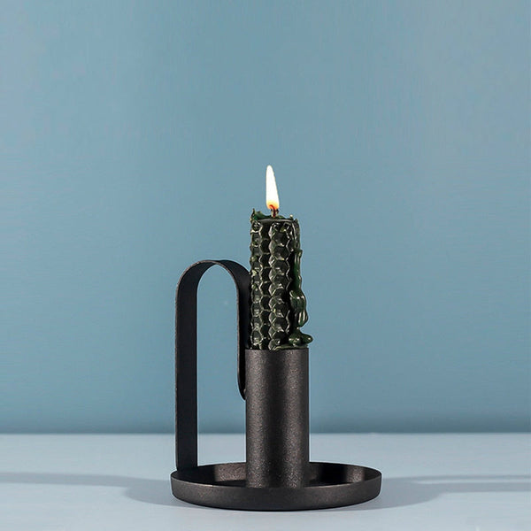 Black iron candle holder with dark green textured candle burning against blue background