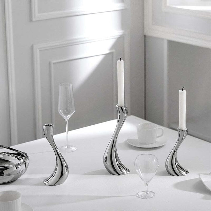 Sculptural ceramic candle holders with white candles on dining table with glass decor