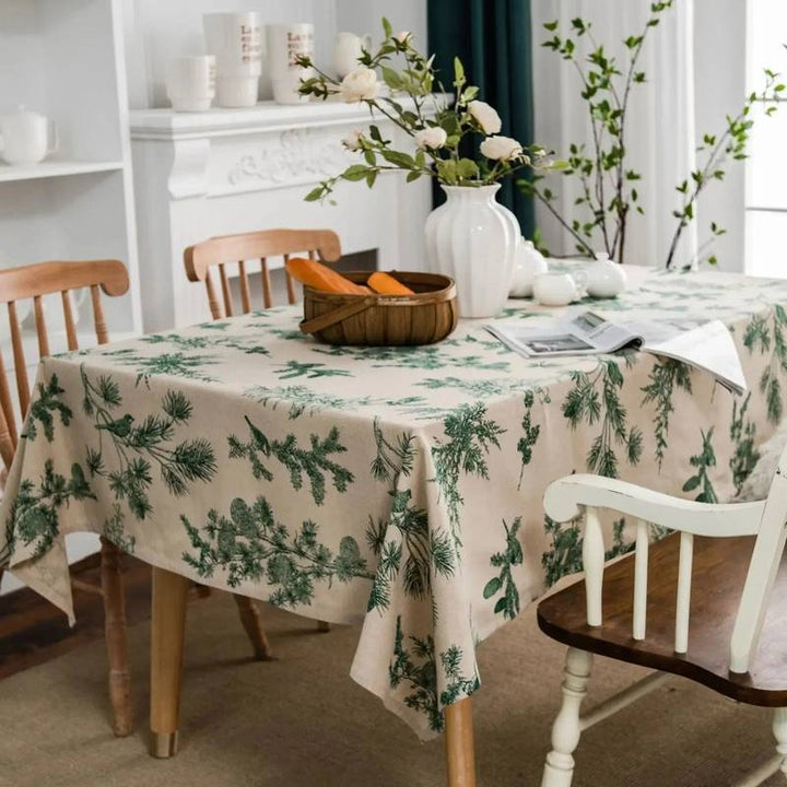Dining room with a table covered by a green leaf-patterned tablecloth, surrounded by wooden chairs.