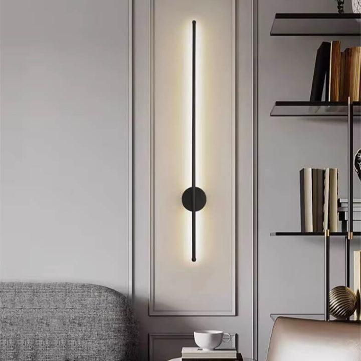 Diagonal black LED wall lamp with circular mount, illuminating a minimalist Nordic living room with clean grey tones