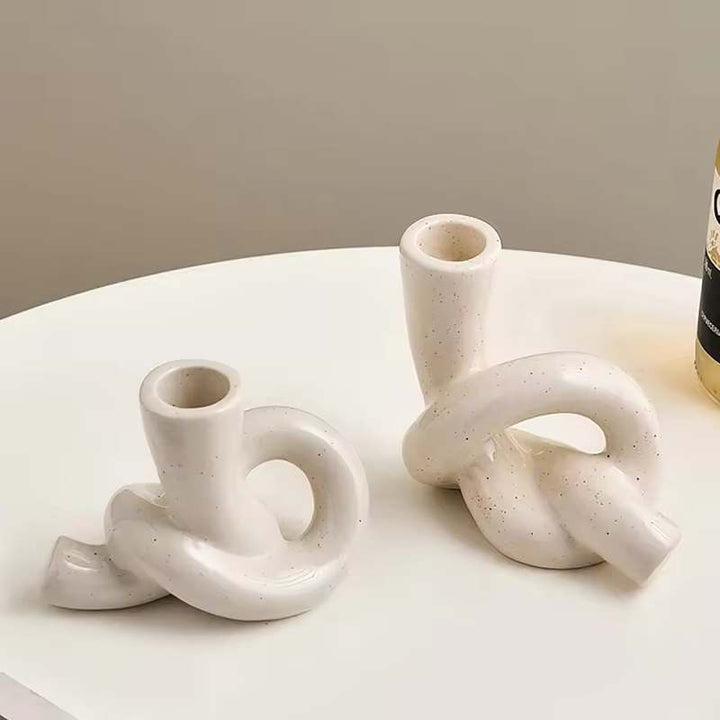 Two white knot-shaped ceramic candle holders on a round table in modern interior