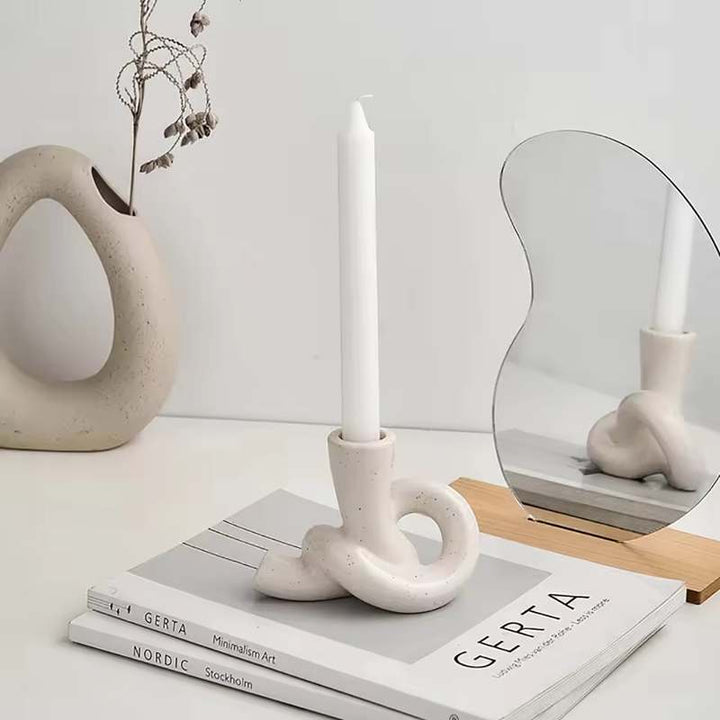 Minimalist ceramic knot candle holder with white taper candle on books and mirror decor
