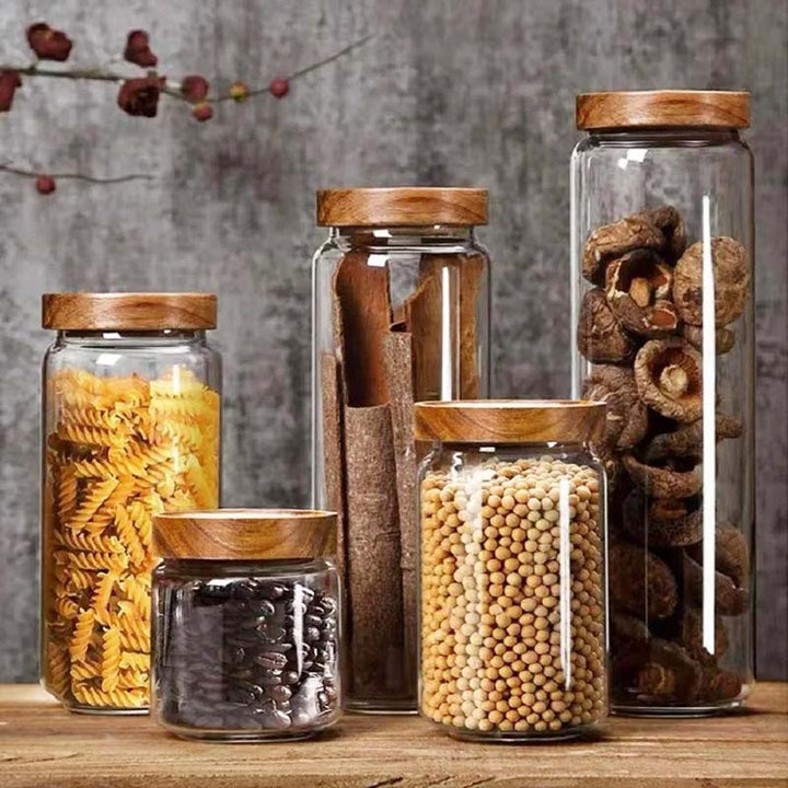 Set of glass jars with wooden lids containing various dry goods on a wooden surface.