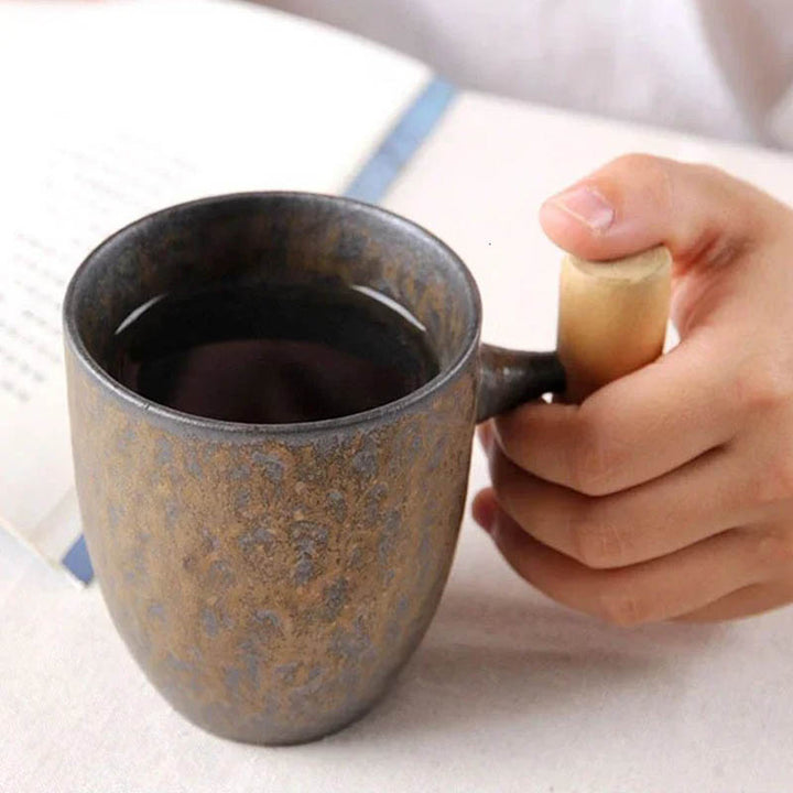 Person holding rustic black ceramic mug with ergonomic wooden handle, ideal for coffee or tea, 300ml UK Nordic Essentials Store