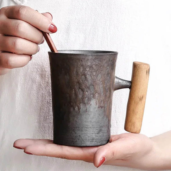 Person holding rustic black ceramic mug with ergonomic wooden handle, ideal for coffee or tea, 300ml UK design